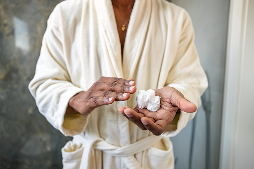 Person in a white bathrobe presenting a dollop of moisturizing cream in their palm, symbolizing self-care and skincare routine.