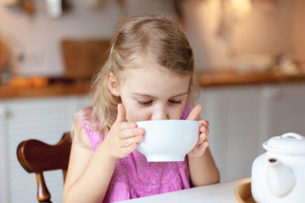 istock Child girl drinks tea at kitchen table. Breakfast with teapot, mug. Cozy home atmosphere. 1951056197