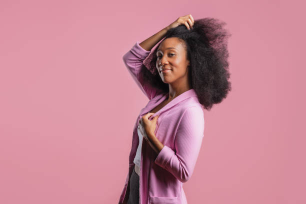 Portrait of a smiling young woman with natural afro hair, wearing a pink blazer over a white shirt, looking confident and stylish.