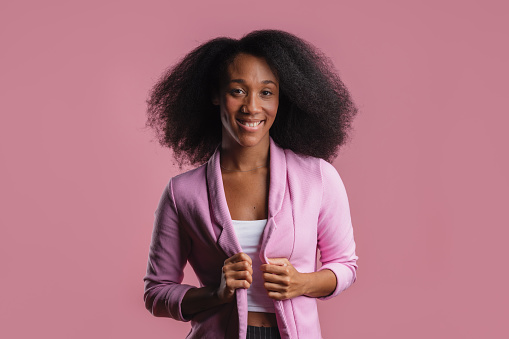 Portrait of a smiling young African-American businesswoman in pink blazer over white top, looking at the camera.