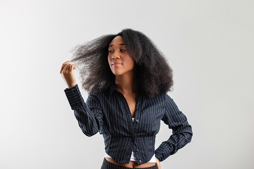 Portrait of a young adult businesswoman with natural hair, standing confidently with hands on hips against a neutral background.