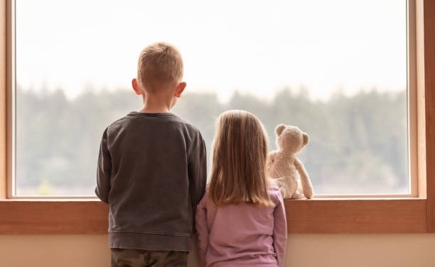istock Brother sister siblings at home looking out window. 1951132359