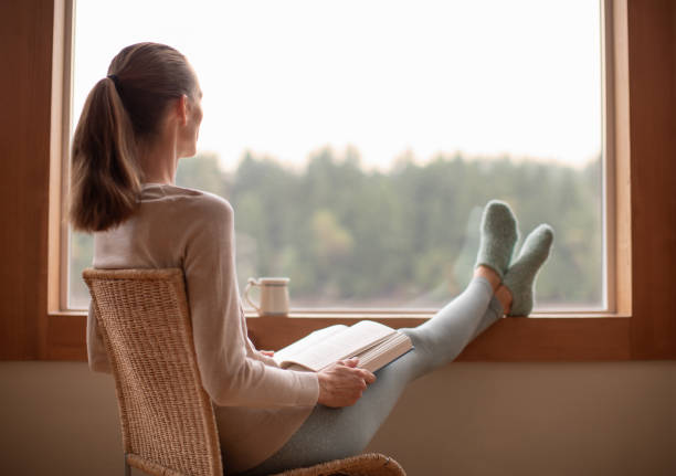 istock Woman sitting by window and reading a book. 1951134939