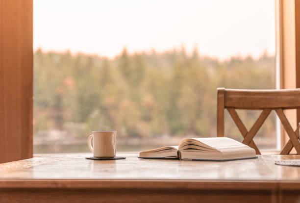 Coffee cup on the table and reading book by a window with relaxing nature view.