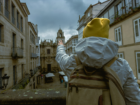 In this evocative image, a solo traveler clad in a white jacket and a yellow beanie waves towards the historic architecture, capturing the essence of solo exploration and the connection between the present traveler and the past.
