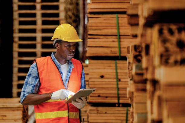 istock African worker carpenter wearing safety uniform and hard hat working and checking the quality of wooden products at workshop manufacturing. man and woman workers wood in dark warehouse industry. 1951256216