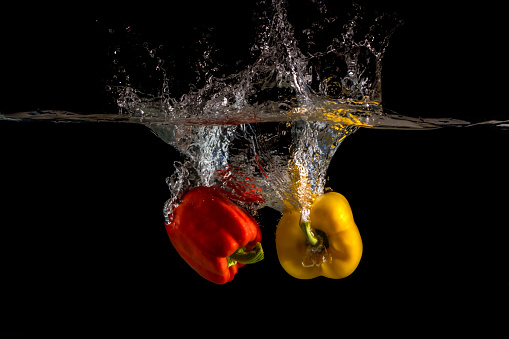 Yellow and red pepper falling into water and splashing against black background