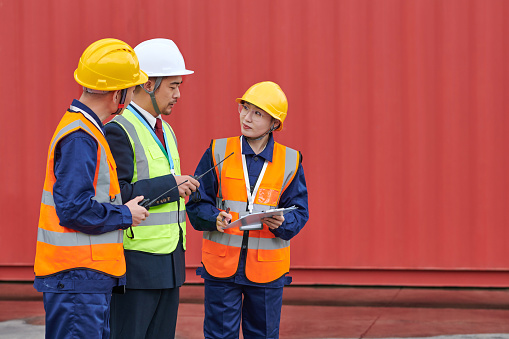 Side view of three asian coworker discussing at loading dock in red cargo container backgrounds.