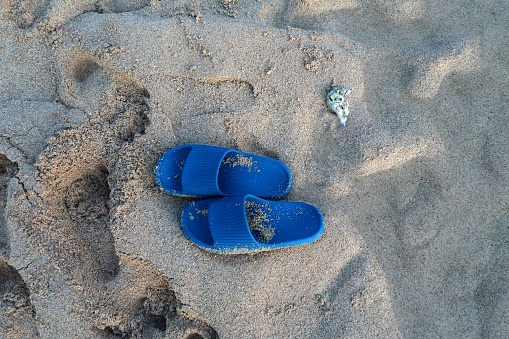 a pair of blue sandals on the beach with beautiful sand. The sandals look natural with traces of human footsteps