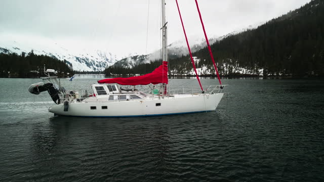 Aerial view orbiting a sailboat parked between snowy mountains of Alaska