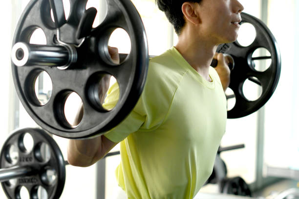 young asian man doing weight training with a barbell at the gym - gym machine smiling coach - fotografias e filmes do acervo