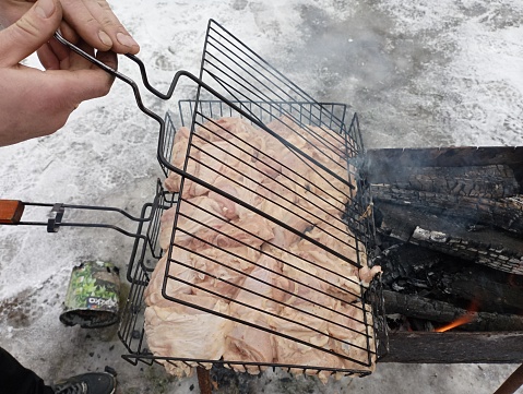 Cooking food on the grill outside. A person closes a net with meat for roasting it on charcoal burning in a barbecue. Relaxation in nature with cooking of meat dishes on an open fire.