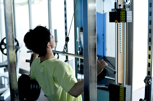 Rear view of a young Asian man doing lat pulldown machine training at the gym