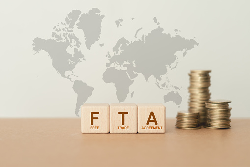 wooden cube blocks with the word FTA,  abbreviation for Free Trade Agreement, and blurred stack of coin on world map background
