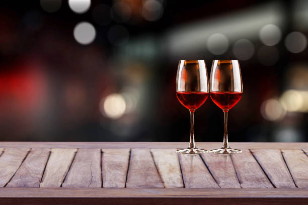 red wine glass on wooden plank with wine bottle rack as background and blurry wine drinking counter background. - wine red wine pouring wineglass fotografías e imágenes de stock