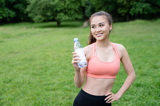 Morning exercise. Sporty and energetic young woman standing on green meadow, holding a water bottle, embracing a healthy and active lifestyle in nature.