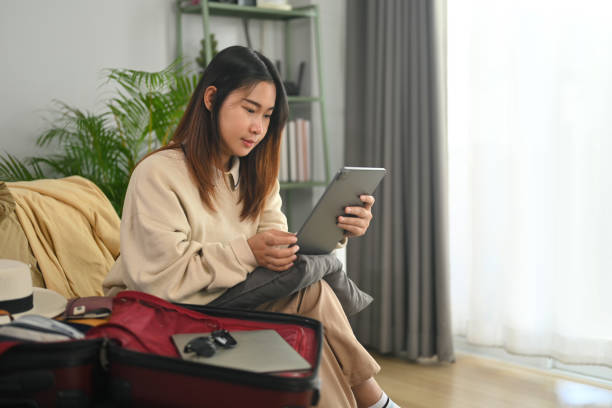 młoda kobieta siedzi na kanapie i szuka zakwaterowania za pomocą serwisu internetowego na tablecie cyfrowym - lodging zdjęcia i obrazy z banku zdjęć