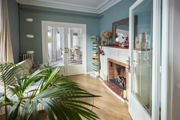 Cozy home interior with French doors Unoccupied living room with sofa, fireplace and mantle, potted plant, book tower, and view into dining room. french doors stock pictures, royalty-free photos & images