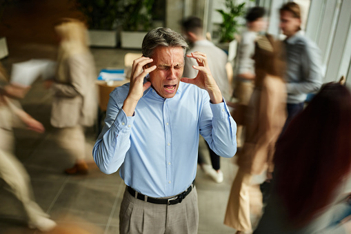 Angry male entrepreneur feeling frustrated while being surrounded by his colleagues who are walking in blurred motion.