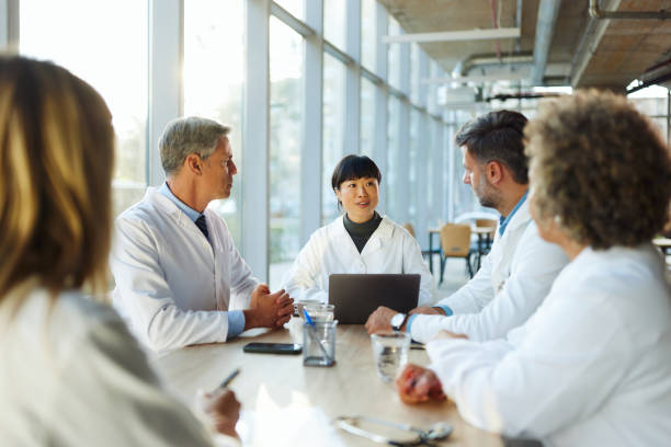 Group of medical practitioners talking on a meeting in hospital. Team of medical experts talking on a meeting at doctor's office. Focus is on Japanese woman. japanese female doctor stock pictures, royalty-free photos & images