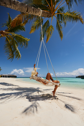 Relaxed woman spending a summer day in a swing on the beach. Copy space.