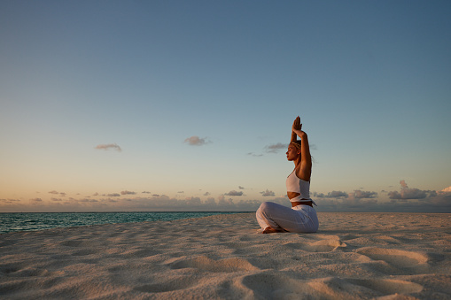 Carefree woman meditating with her arms raised during summer on the beach. Copy space.