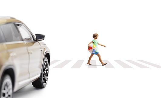 Full length profile shot of a boy crossing a street and carrying a beach ball