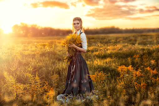 Beauty Romantic Autumn Girl Outdoors. Beautiful Teenage Model girl in Long Dress Posing on the Field in Sun Light. Attractive young woman portrait