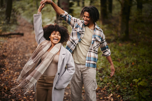 Carefree African American couple having fun while dancing during autumn day in the forest.