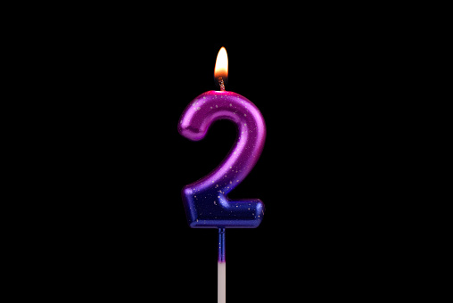 Burning colorful birthday candle isolated on black background. Number 2.