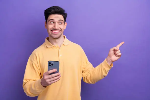 Photo of charming cute man dressed yellow shirt texting apple iphone samsung device showing empty space isolated purple color background.