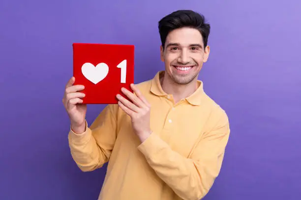 Photo of Photo of excited positive man dressed yellow shirt rising feedback like heart card isolated purple color background