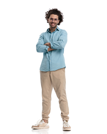 joyful young casual man standing on white background with arms folded and smiling