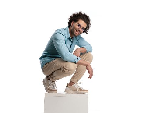 casual man wearing glasses and blue shirt leaning forward while standing on crate on isolated background