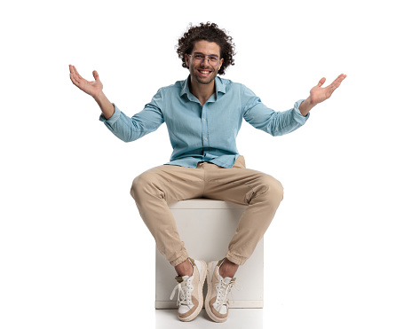 seated handsome casual man making welcoming gesture on white background