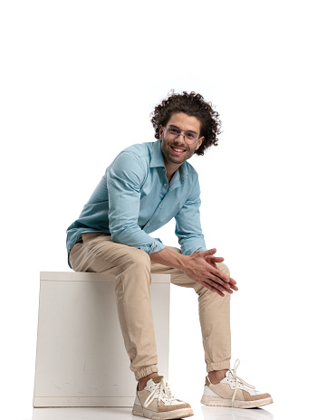 young casual man relaxing while sitting on a chair and smiling on isolated background