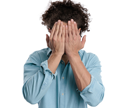 closeup of unhappy casual man wearing blue shirt covering his face on isolated background