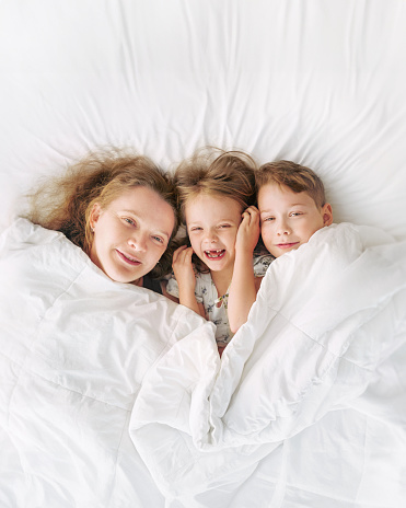 Happy family - portrait of children and mother in bed. Happy, love and fun at home. Family, childhood.