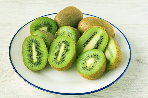 On a white plate on the table there is a fresh healthy kiwi cut in half.