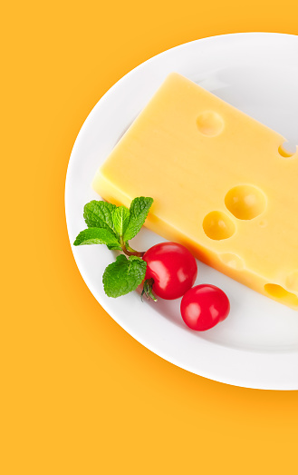 Yellow cheese with red tomatoes and green mint leaves on the white plate. Organic natural food ingredients yellow background.