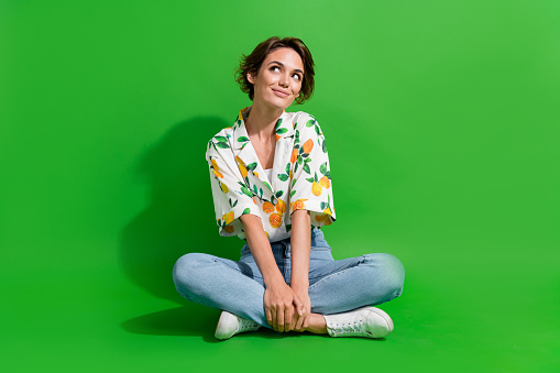 Full body photo of young woman sitting floor looking thoughtful wondered spend money on black friday isolated over green color background.