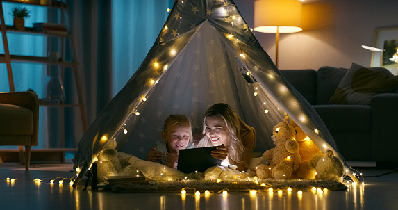Happy, home and mother with girl, tablet and bonding together with love, internet and cartoon. Family, mama and kid with technology, social media and relax in a living room, tent and online movie