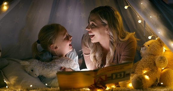 Mom, daughter and tent with book, night and lights for reading on living room floor. Happy, learning and education in evening, story time and together for holiday, house and parenting for bedtime