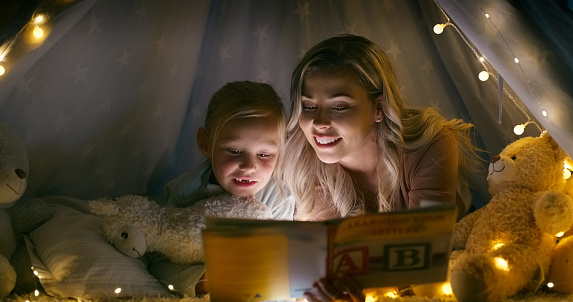 Reading book, child and fort with mother at night in family home with love, bonding and development. Story, mom and young girl with education, smile and happy together with care and fantasy tale