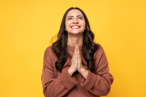 Portrait of crying young woman makes imploring expression keeps palms pressed together asks for favor says please looking at camera with hope, standing on white isolated background in studio.