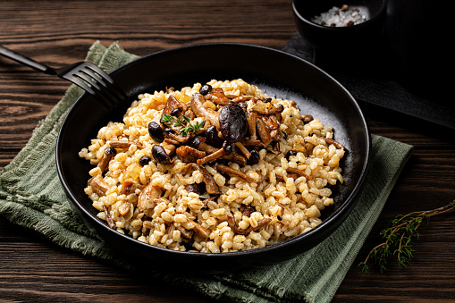 Mushroom barley risotto or orzotto in a black plate. Made with pioppini and porcini mushrooms. Vegan food.