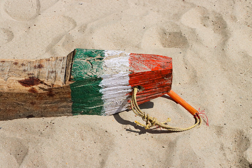 Stock photo showing elevated view of a rustic,  wood block used for mooring  fishing boats on sandy beach. The wood chock is painted with saffron (orange), white and green stripes like the National flag of India (tricolour).