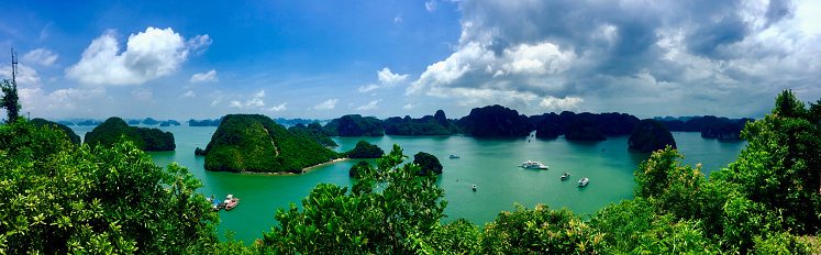 Hạ Long Bay, Vietnam, featuring emerald waters, limestone islets, and lush greenery, with boats and white clouds under a blue sky, highlighting its role as a tourist attraction. Taken in 2016.