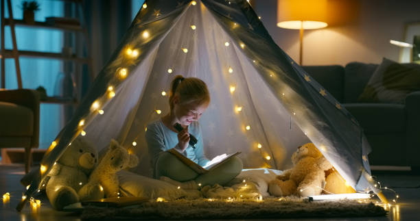 istock Torch, teddy bear and kid reading a book in a blanket fort for bed time routine and knowledge. Smile, toy and girl child enjoying a story or novel for education with light in tent in bedroom at home. 1952000358