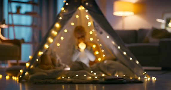 Child, teepee tent and home play for fun fantasy game or development, camping or entertainment. Person, blanket and fort in living room for imagination at night or fairy lights, holiday or weekend